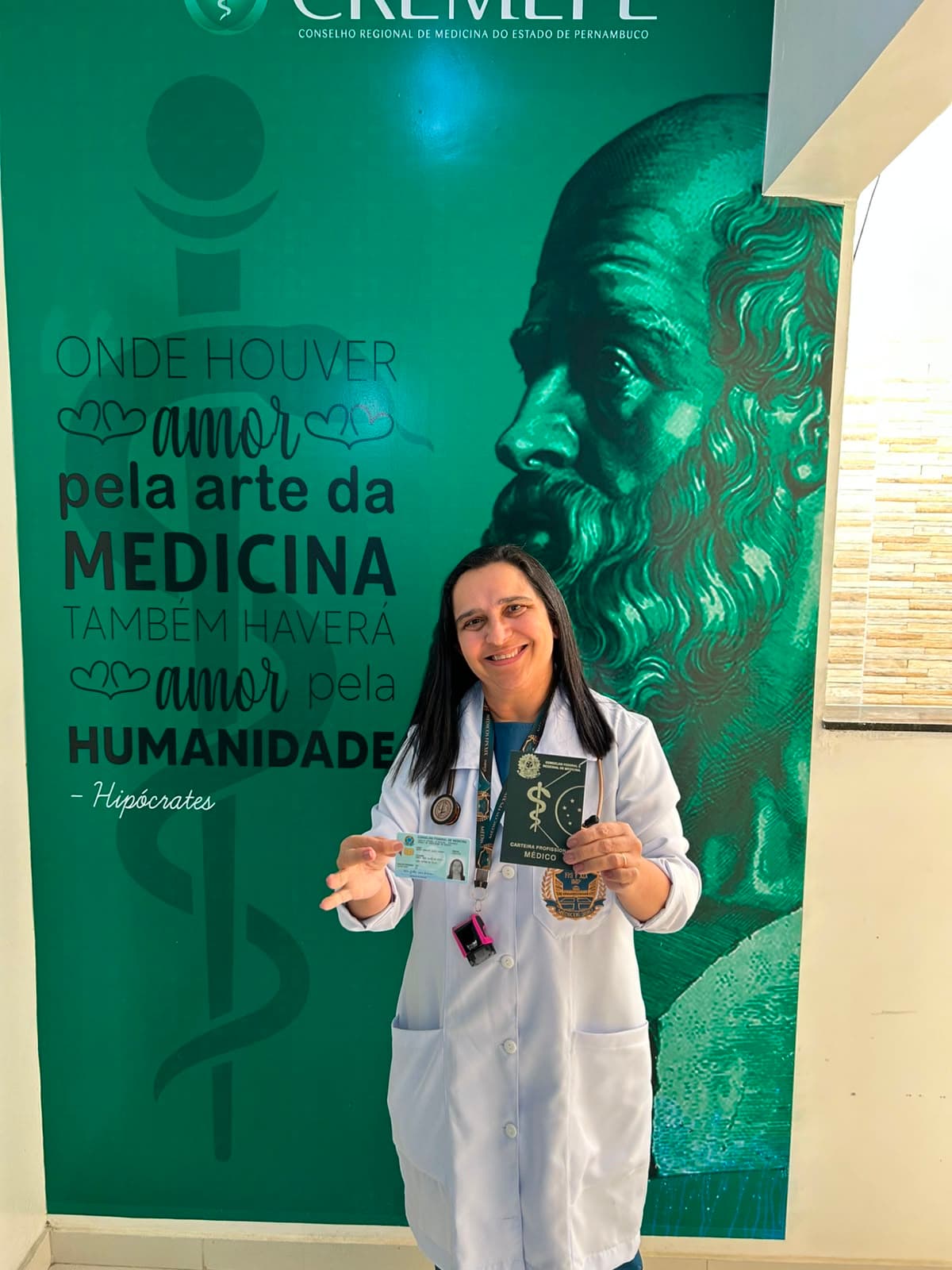 Maria Gorethe Alves Lucena, de jaleco branco, segurando a carteira profissional de médica no CREMEPE.